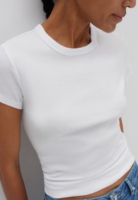 T-shirt bianco a maniche corte con scollo rotondo, caratterizzato da un design aderente e una consistenza morbida, abbinato a jeans blu in denim.