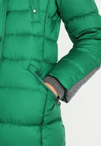 Grön puffjacka med dragkedjefickor, smidigt material, kviltat mönster och grå stickade manschetter.