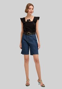 Top corto nero a maniche corte con spalle arricciate, pantaloni corti in denim blu, cintura nera con fibbia rotonda e sandali verdi con tacco.