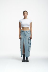 Denim cargo szoknya oldalsó zsebekkel, középmagas szárú, világoskék mosású, elöl hasított, fehér rövidített pólóval és fekete bokacsizmával párosítva.