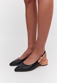 Scarpe slingback in pelle nera con punta affilata e un accento pesca a contrasto sul tacco, caratterizzate da un dettaglio decorativo a fiocco.