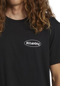 Czarna bawełniana koszulka z krótkim rękawem, z białym owalnym logo z napisem "Billabong". Okrągły dekolt. Miękka faktura.