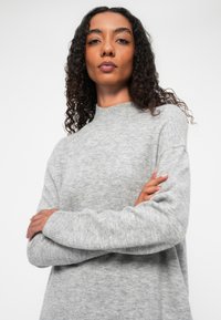 Maglione grigio in lana con un collo alto, vestibilità comoda e polsini a costine. Il tessuto sembra morbido con un motivo testurizzato su tutta la superficie.