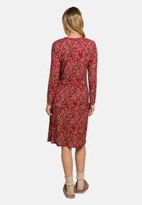 Rotes langärmliges Kleid mit floralem Muster, knielanger Saum, runder Ausschnitt und weichem, strukturiertem Stoff. Kombiniert mit hellen, gemütlichen Socken.
