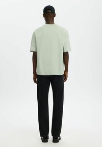 T-shirt vert clair à manches courtes avec une coupe décontractée, associé à un jean droit bleu foncé et des chaussures noires, vu de dos.