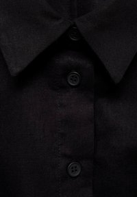 Camicia in lino nera con colletto classico, cinque bottoni neri sul davanti e un primo piano del tessuto testurizzato.