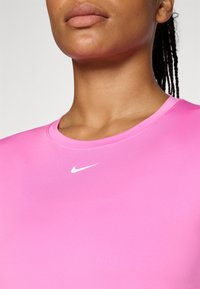 Kortermet, rundhalset treningsgenser i lys rosa stoff. Har en liten hvit Nike-logo på brystet. Glatt tekstur.