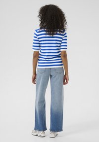 Blauw-wit gestreepte short-sleeve top, gecombineerd met licht gewassen, wijde jeans en witte sneakers, gezien vanaf de achterkant.