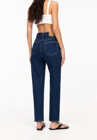 Vaqueros de denim azul oscuro de cintura alta con un corte relajado, que cuentan con dos bolsillos traseros y costuras en contraste. Textura de tela suave.