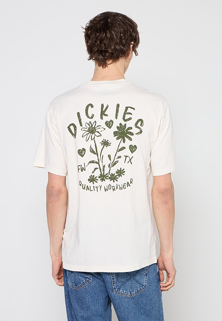 Mann trägt weißes Kurzarm-T-Shirt mit grünem Blumendesign und dem Text "Dickies FW TX Quality Workwear" auf der Rückseite, kombiniert mit blauen Jeans.