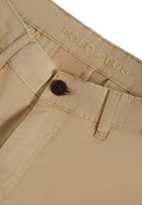 Beiga bomullschinos med en mjuk textur, med en brun knappstängning och broderad "POLO CLUB"-logotyp på midjebandet.