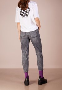 Camiseta gráfica en blanco y negro, jeans desgastados grises, zapatos de plataforma negros, calcetines morados, vista desde la parte trasera. Tejido suave, corte casual.