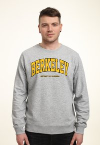 Felpa grigia con scollatura arrotondata e polsini a coste, con "BERKELEY" e "UNIVERSITY OF CALIFORNIA" stampati in bold giallo.