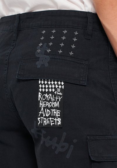 Schwarze Cargo-Hosen mit strukturiertem Finish, versehen mit gestickten Kreuzen, einem Etikett mit weißem Text und einer Taschenklappe.