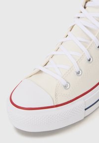 Beige canvas sneakers med vita snören, gummitåhätta och röda samt blå detaljer längs sulan. Strukturerad sula för bra grepp.
