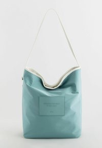 Light blue slouchy bag made of durable material, featuring a cream trim, embossed logo patch, and a single shoulder strap.