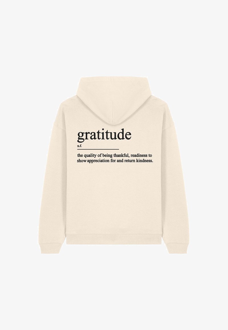 Felpa crema con cappuccio e cordoncino. Sul retro è presente la parola "gratitudine" in grande carattere nero, con una definizione in carattere più piccolo sottostante.