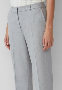 Pantalons taillés gris en tissu texturé avec un devant plat, des poches latérales et une coupe droite. Lignes épurées et détails subtils.