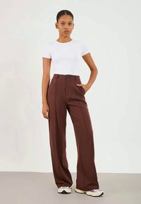 Brown wide-leg trousers with front pockets, a button closure, and a smooth fabric texture, paired with a fitted white t-shirt.