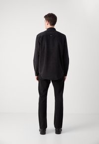 Camisa de cordón negra con mangas largas, puños abotonados, dobladillo recto y una textura sutil. Combinada con pantalones negros y botines.