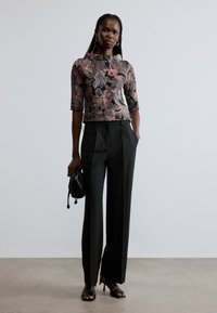 Floral-patterned, fitted top in black and pink, paired with high-waisted, wide-legged black trousers and strappy black heels.