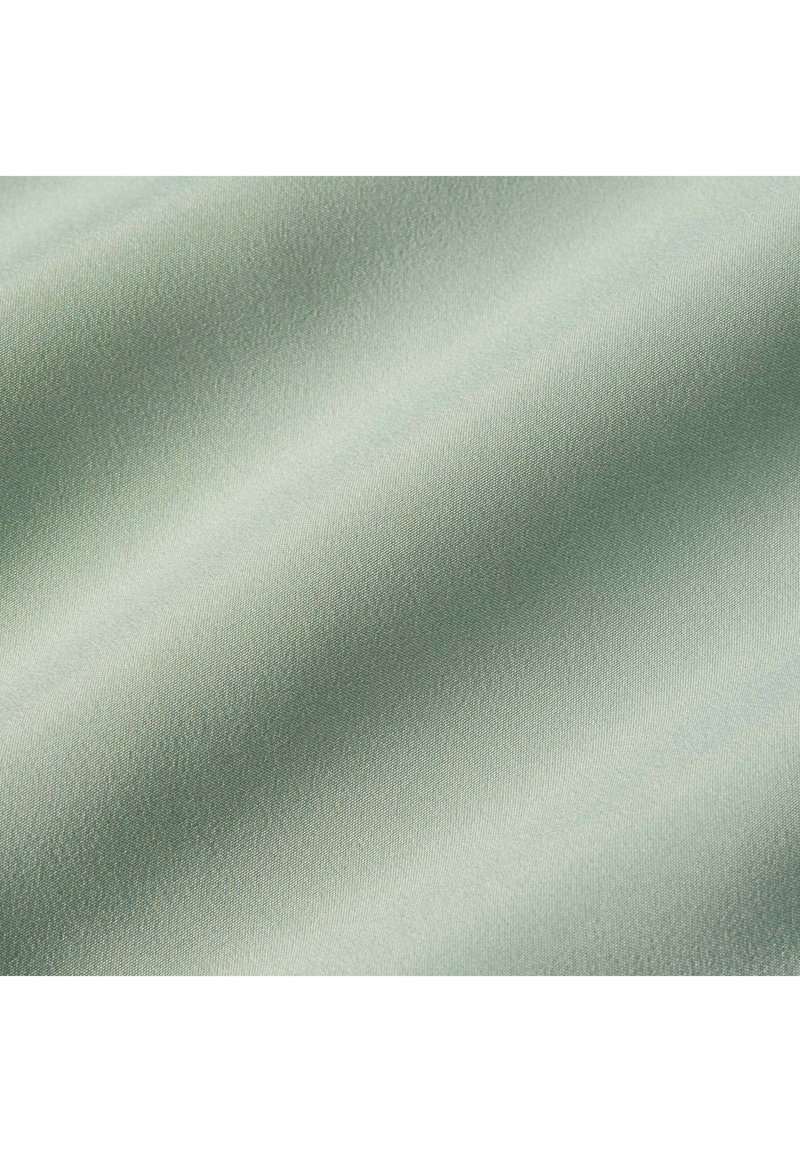 Tissu vert clair lisse avec un léger éclat et une texture tissée fine, présenté en gros plan avec de douces plis.