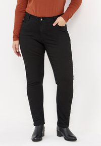 Svarta denim skinny jeans med hög midja, smal passform och framfickor. I kombination med en orange långärmad topp och svarta klackboots.