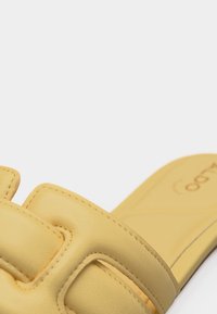 Gros plan d'une sandale beige à enfiler avec des brides rembourrées et des coutures détaillées sur un fond uni.