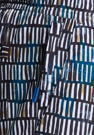 Vzorovaná tkanina s vertikálními černými, bílými a modro-zelenými pruhy, s modrým zipovým kováním a texturovanými akcenty. Detailní záběr na oblast kapsy.