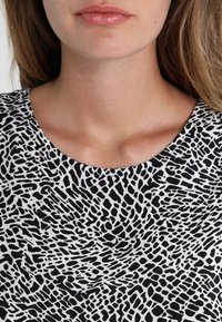 Czarno-biała bluzka z okrągłym dekoltem i fakturowanym wzorem przypominającym abstrakcyjny print zwierzęcy na całej tkaninie.