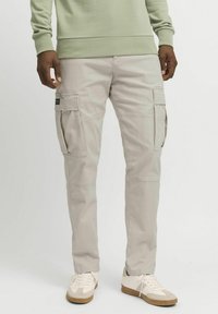 Beige cargobukser med sidelommer, innsnevret passform og lett bomullsmateriale. Brukes med hvite joggesko og en lys grønn genser.