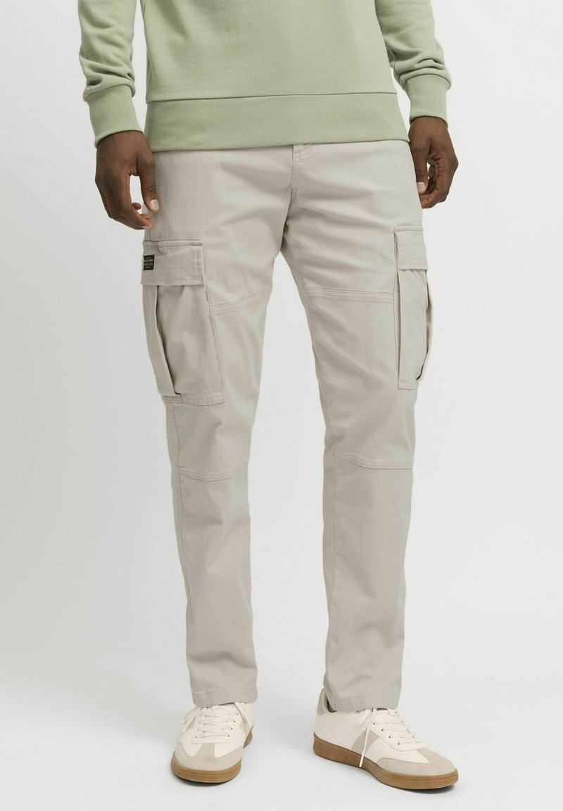 Beige cargobukser med sidelommer, innsnevret passform og lett bomullsmateriale. Brukes med hvite joggesko og en lys grønn genser.