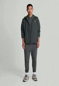 Lätt mörkgrå zip-up jacka med huva, ihop med en matchande grå polo och joggers, komplett med beige sneakers och vita strumpor.