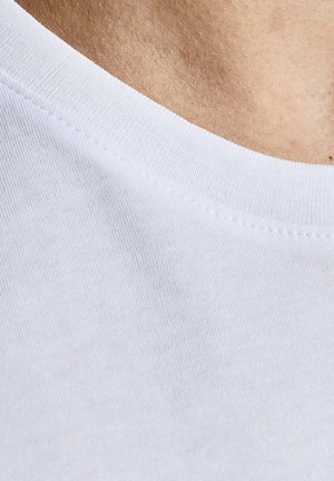 Close-up van witte T-shirtstof met ronde hals en stiksels op de schouder en de bovenste borst van een persoon.