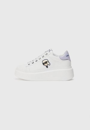 White platform sneakers with a leather upper, featuring a black and white logo patch, silver eyelets, and a lavender heel accent.
