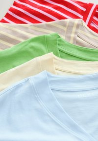 Fem T-shirts i forskellige farver: rød med hvide striber, grøn, bleg gul, beige med lys striber og lyseblå med V-hals design.