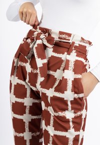 Hooggetailleerde broek met een strikriem, voorzien van een gedurfde bruine en crèmekleurige geometrische patroon, gladde stof en zijzakken.