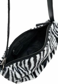 Sac bandoulière en fausse fourrure à rayures noires et blanches avec une fermeture éclair, doté d'un intérieur en tissu noir et d'une bandoulière en cuir.