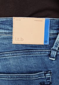 Traperice sa svijetloplavom etiketom na pojasu, s utisnutim natpisom "l.t.b" i plavim naglaskom na etiketici. Tekstura tkanine je srednjeg pranja.