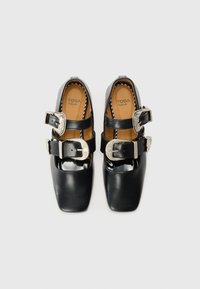 Black leather shoes with square toes, patent accents, and two adjustable buckles in silver. Interior features tan lining and branding.