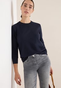 Marineblaue Strickpullover mit Rundhalsausschnitt und dreiviertellangen Ärmeln, kombiniert mit hellgrauen Jeans. Glatte Textur, lässige Passform.