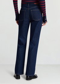 Jean large bleu foncé en denim, avec deux poches arrière et coutures contrastantes. Associé à des chaussures noires.