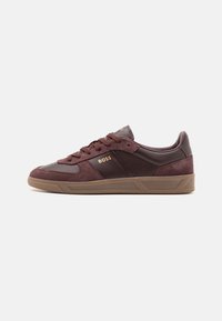 Bordeauxfarbene Wildleder- und Leder-Sneaker mit strukturierter Oberfläche, goldenen Logo-Details und einer Gummisohle mit geometrischem Muster.