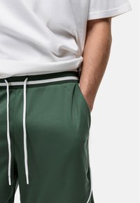 Groene mesh shorts met een witte trekkoord en zijstrepen, voorzien van een ontspannen pasvorm en voorzakken. Gecombineerd met een gewone witte t-shirt.