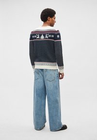 Námornícky pletený sveter s vianočným vzorom, obsahujúci soby a vločky, v kombinácii so svetlomodrými džínsami s širokými nohavicami. Mäkká textúra, ležérny strih.