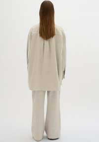 Beige strukturiertes Outfit, bestehend aus einem langärmeligen Oberteil und einer locker sitzenden Hose, mit einem gerippten Muster und vorderen Taschen.