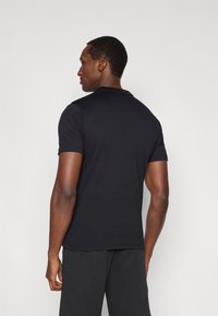 Fekete rövid ujjú póló kerek nyakkivágással, puha anyagból készült, testhezálló szabással és sima textúrával, sötét nadrággal viselve.