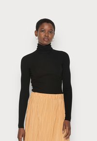 Schwarzer gerippter Rollkragenpullover mit langen Ärmeln, kombiniert mit einem plissierten, knielangen, hellbeigen Rock. Minimalistisches Design und weiche Textur.