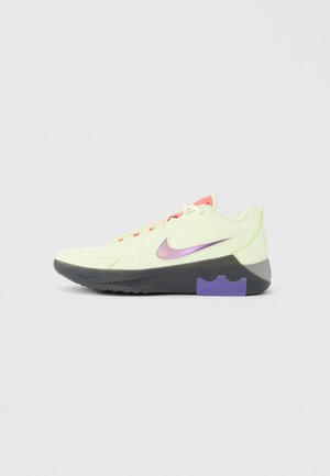 Sneaker basso con tomaia giallo pallido, swoosh Nike metallico viola, suola nera e dettaglio viola nella sezione del tallone.