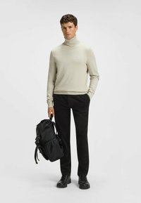 Jasno-beżowy sweter z golfem, dopasowany krój, gładka tekstura; zestawiony z czarnymi spodniami w kord w i czarnym plecakiem z regulowanymi ramiączkami.